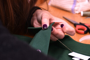 woman sewing with needle and thread a button on a green t-shirt - obrazy, fototapety, plakaty