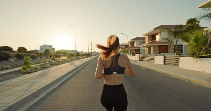 Caucasian woman jogging on the street near the house. a beautiful sporty active girl with a healthy lifestyle is running on the asphalt. High quality 4k footage