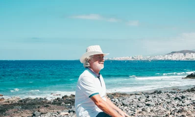 Deurstickers Canarische Eilanden Happy white-haired senior man enjoying sea vacation sitting at the beach in a sunny day