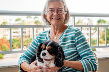 Portrait of senior woman sitting on the home balcony holding her cavalier king charles dog on the...