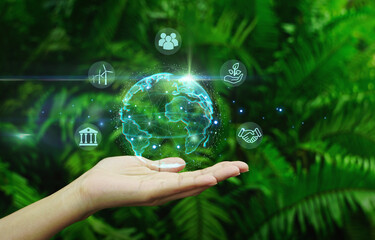 Hand holding digital earth globe with ESG smart icon around it on green natural leaf...