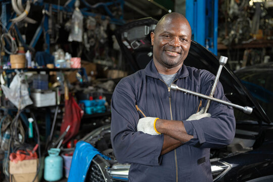 mechanic crossed arms pose and holding lug wrench for fixing a car in automobile repair shop