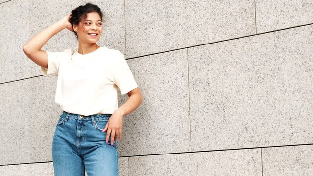 Young beautiful smiling hipster woman in trendy summer jeans and white t-shirt clothes. Carefree model posing in the street near wall. Positive brunette female. Cheerful and happy