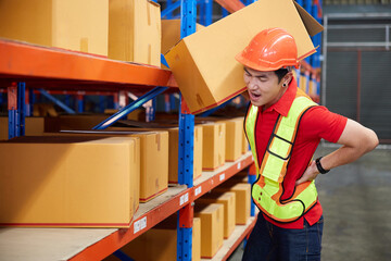 factory worker holding corrugated boxes and suffering back pain beside shelf in the warehouse...