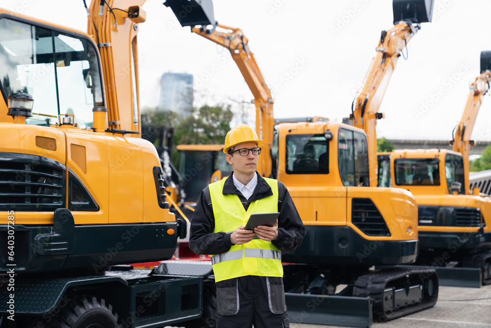 Aufkleber engineer in a helmet with a digital tablet stands next to construction excavators.