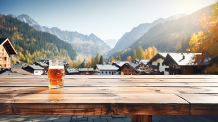 Wooden table top showcase with mug of beer on alpine village background, holiday flags, blank bokeh background