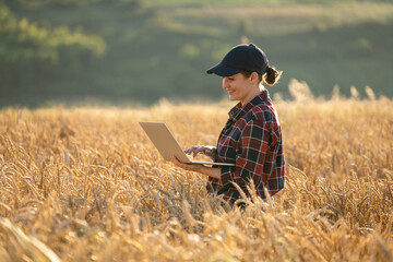 Woman farmer working with laptop on wheat field. Smart farming and digital agriculture