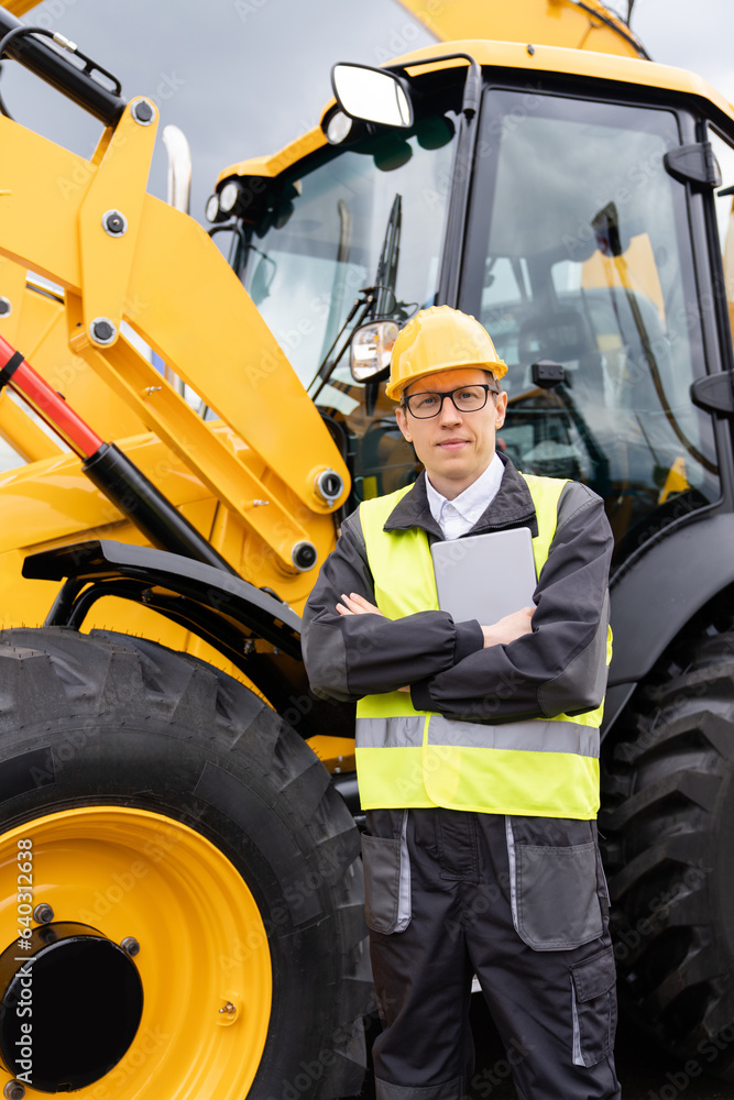 Poster Worker in a helmet with a digital tablet on the background of construction machine.