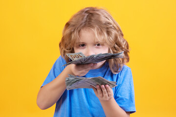 Money win, big luck. Kid with lots of money dollar banknotes isolated over yellow studio background.