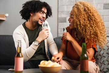 Couple in love sings karaoke on sofa in living room at home