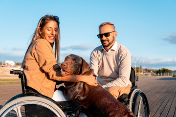 Care with pet, like family. Cheerful woman using wheelchair with boyfriend petting dog in bright...