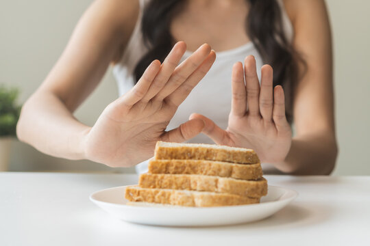 Gluten allergy, asian young woman hand push out, refusing to eat white bread slice on plate in breakfast food meal at home, girl having a stomach ache. Gluten intolerant and Gluten free diet concept.