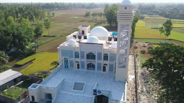 Drone shot circling Bangladesh's stunning holy model mosque in the midst of woods and rice fields, beside road