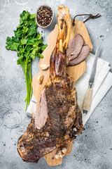 Whole roast mutton lamb leg with spices on a wooden board. Gray background. Top view