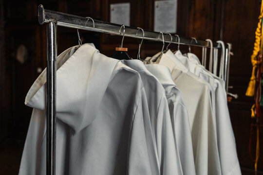 White priest's tunics hanging. Benedictine albs in cotton arranged in a row inside a sacristy.