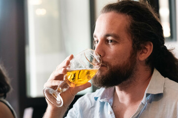 Man with long hair and beard drinks beer. Portrait of Caucasian man sipping lager in a bar....
