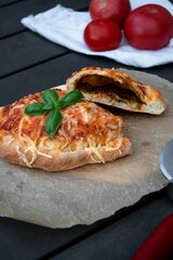 Close up of cutted pizza calzone with tomato sauce, green pesto and cheese on wooden plate
