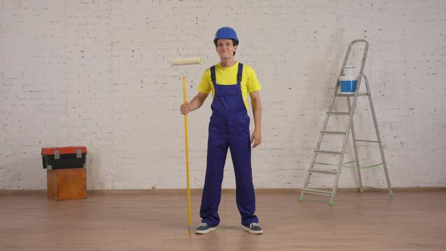 Full length video of a smiling young worker standing in the room with a roller, looking at freshly painted walls and giving a thumbs up.