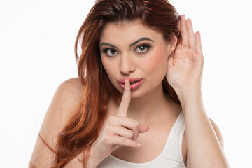 Redhead woman holds her hand near ear and listens carefully with silence gesture isolated on white background