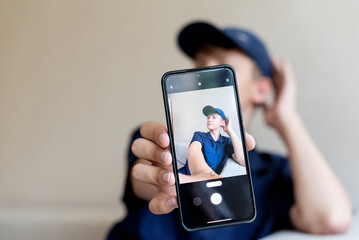 teenage boy holding a smart phone in front of his face at home, taking selfies with his smartphone, digital display on foreground, teen with his own portrait in smartphone, teen blogging