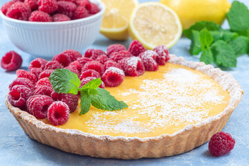 Lemon tart, garnished with fresh raspberry, icing sugar, mint, horizontal