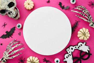 Wishing you a hauntingly good time at Halloween party. Top view of skeleton hands, skull, ghostly eyewear, pumpkins, creepy eyes, eerie insects on pink background with blank circle for ad or text