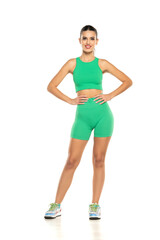 young sporty smiling woman in green shorts and top posing on white background