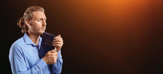 Praying young man with Holy Bible on dark background with space for text