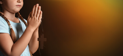 Praying little girl with cross on dark background with space for text