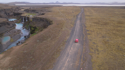 AERIAL - Jeep driving off-road terrain exploring Sigoldugljufur, a canyon in the Icelandic Highlands. A 4x4 jeep driving dirt road traveling in Iceland sightseeing wilderness. woman traveler waving.