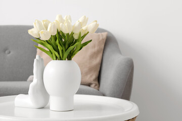 Vase with beautiful tulip flowers on table near grey sofa