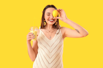 Young woman with glass of smoothie and lemon on yellow background