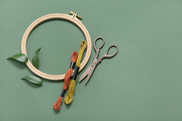 Wooden embroidery hoop with mouline threads, scissors and leaves on dark green background © Pixel-Shot