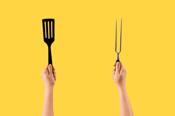 Female hands holding spatula and carving fork on yellow background