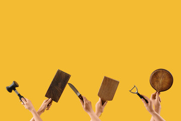 Female hands holding cutting board and different kitchen utensils on yellow background