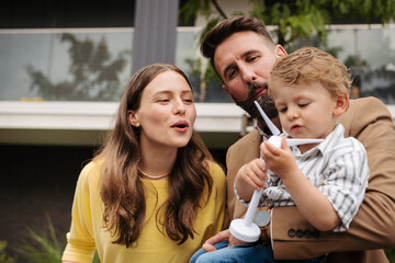 Smiling parents with little son blowing on wind turbine model.