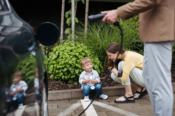 Man unplugging their electric car from charger on the street, while wife and son waiting for him.
