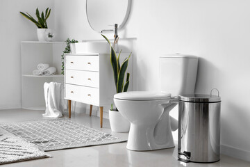 White toilet bowl and metallic trash bin in interior of light bathroom - obrazy, fototapety, plakaty