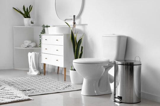 White toilet bowl and metallic trash bin in interior of light bathroom