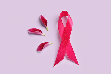 Composition with pink awareness ribbon and flower petals on color background. Breast cancer concept