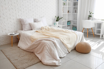 Interior of light children's bedroom with cozy bed, shelving unit and desk near window