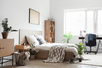 Interior of children's bedroom with cozy bed, shelving unit, desk and houseplants