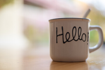 Cup of hot coffee on a wooden table outside the house with a message with the word Hello. Image with copy space. Close-up