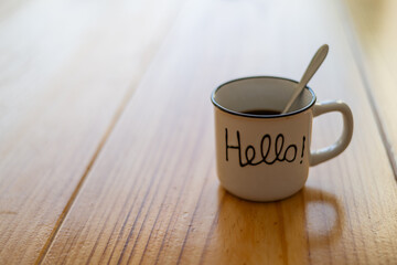 Cup of hot coffee on a wooden table outside the house with a message with the word Hello. Image with copy space.