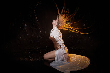 Fototapeta premium Beautiful sexy skinny girl and her flying hair in a dark hall with splashes of water. Female Model blonde woman posing with water on a black background in the studio