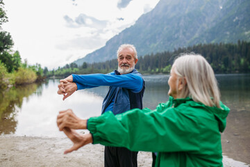 Senior couple doing outdoor yoga by the lake in the mountains.