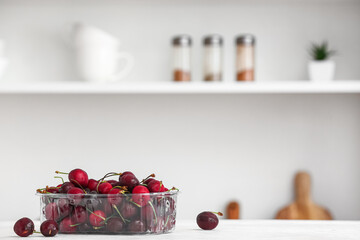 Plastic container with ripe cherries on table in kitchen