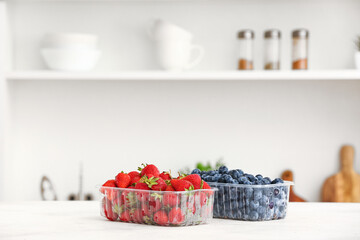 Plastic containers with ripe berries on table in kitchen