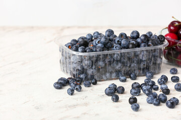 Plastic container with ripe blueberries on table in kitchen