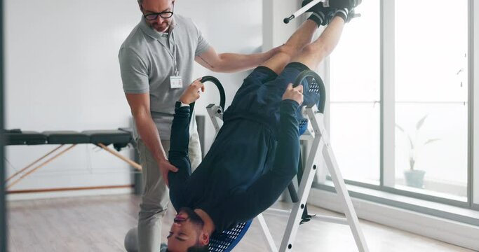 Chiropractor, equipment and patient with back pain stretching on inversion table for healing spinal muscle in healthcare clinic. Spine, injury and man in physiotherapy rehabilitation with doctor